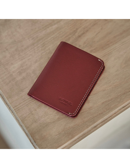 Portefeuille pour homme en cuir petit avec porte-billets couleur bordeaux, vue de face inclinée sur une table - MONPIEL