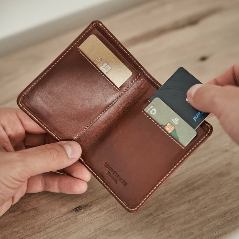 Small Havana leather men's wallet with billfold, open in hand with card details and a table background - MONPIEL