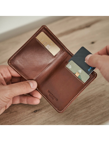 Small men’s leather wallet with billfold in Havana, open in hand with card details and table background - MONPIEL Small men’s leather wallet with billfold in Havana, open in hand with card details and table background - MONPIEL