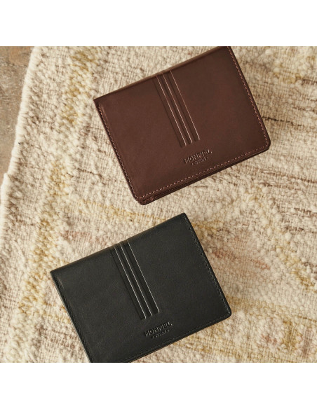 Leather wallet with clasp inside and coin pocket in black and brown with front view on a rug - MONPIEL
