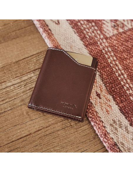 Brown leather pocket wallet, shown from the front and slightly tilted on a wooden table - MONPIEL Brown leather pocket wallet, shown from the front and slightly tilted on a wooden table - MONPIEL