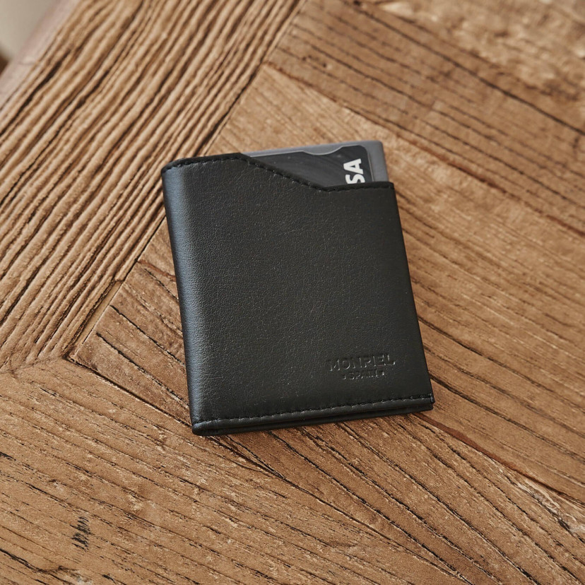 Black leather pocket wallet, shown from the front and slightly tilted on a wooden table - MONPIEL