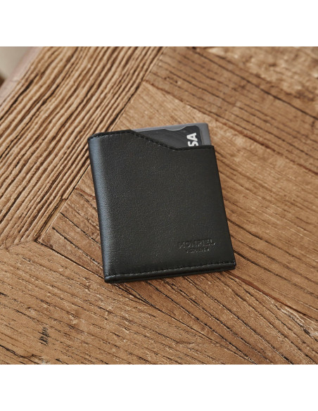 Cartera pocket de piel en color negro con vista frontal y ligeramente inclinada sobre una mesa de madera - MONPIEL Cartera pocket de piel en color negro con vista frontal y ligeramente inclinada sobre una mesa de madera - MONPIEL