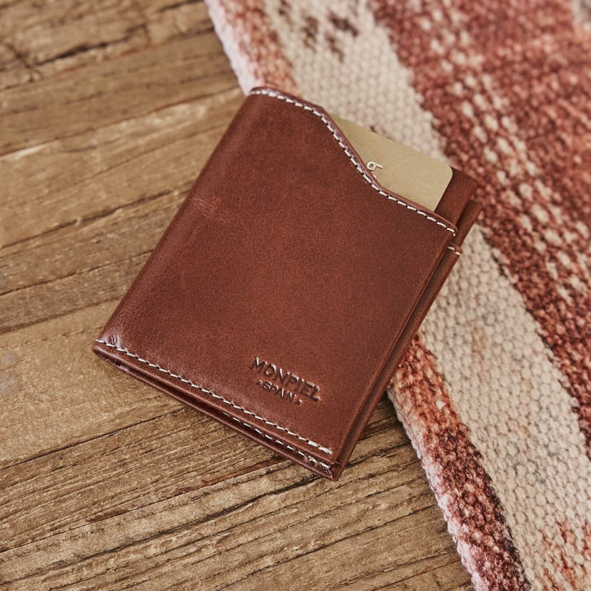 Tan leather pocket wallet, tilted on a wooden and fabric table - MONPIEL