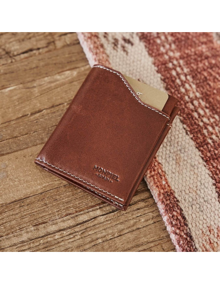 Tan leather pocket wallet, tilted on a wooden and fabric table - MONPIEL Tan leather pocket wallet, tilted on a wooden and fabric table - MONPIEL
