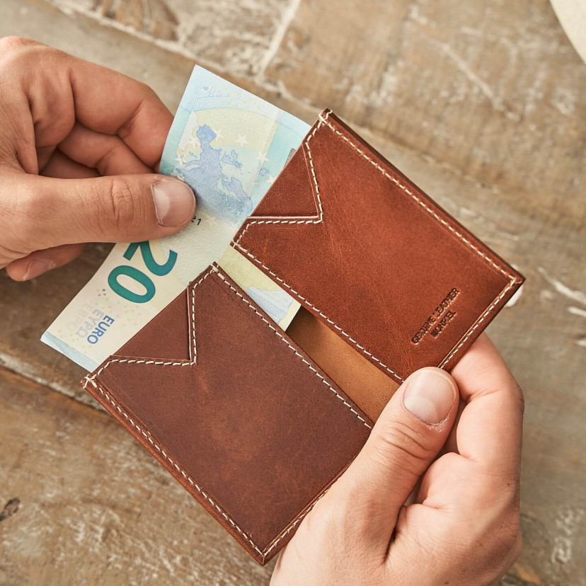 Small Havana leather men's wallet, open and held in hands with a table background - MONPIEL