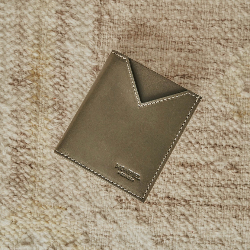 Small green leather men's wallet, shown from the front resting on a carpet - MONPIEL