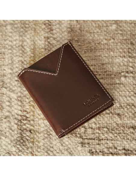 Small men's leather wallet in brown, front diagonal view resting on a rug - MONPIEL Small men's leather wallet in brown, front diagonal view resting on a rug - MONPIEL