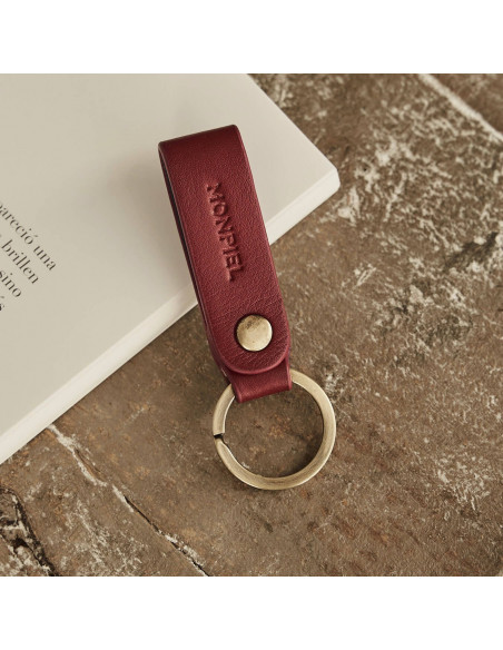 Bordeaux bicolor leather pocket keychain, resting on a magazine and wooden table - MONPIEL Bordeaux bicolor leather pocket keychain, resting on a magazine and wooden table - MONPIEL