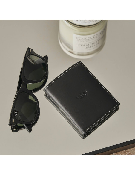 Simple black leather billfold with central logo, resting on a mirror with sunglasses beside it - MONPIEL