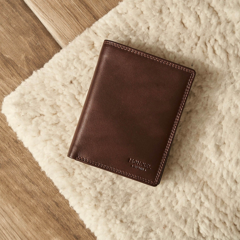 Brown leather wallet with double stitching, shown from the front and slightly tilted, resting on a carpet - MONPIEL