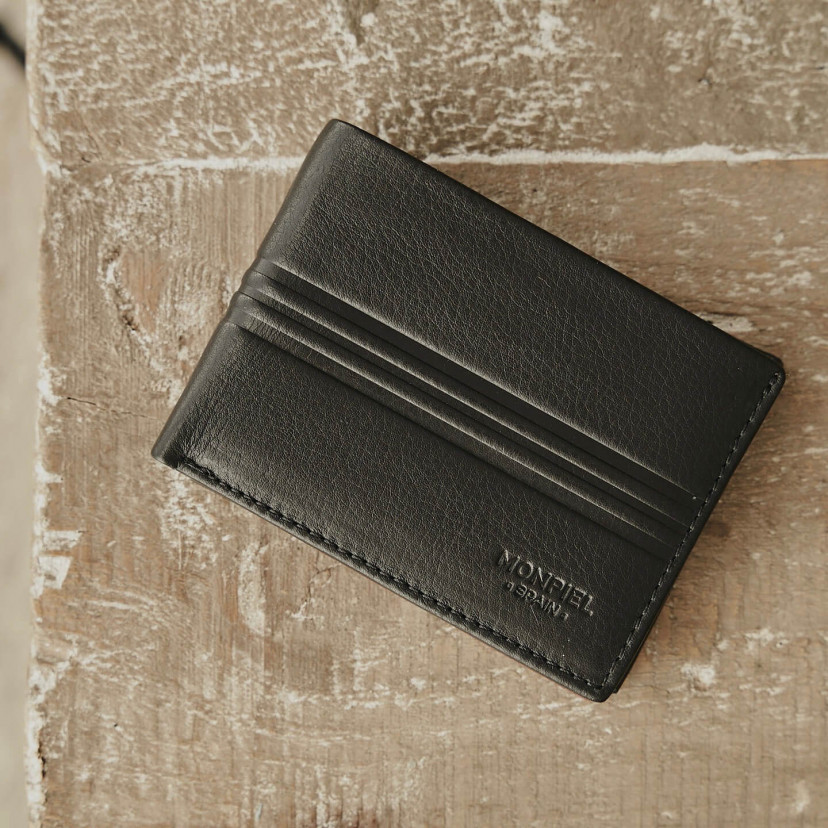 Small American-style leather wallet with coin pocket in black, front view, on a wooden table - MONPIEL
