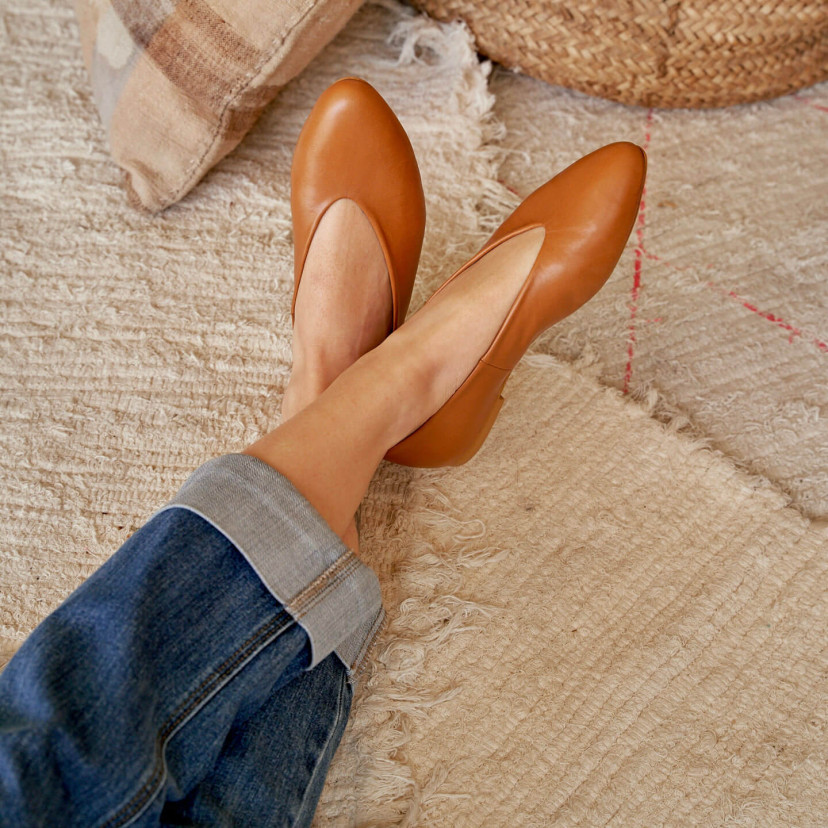 Flat ballerina in tan color, feet crossed and resting on a rug - MONPIEL