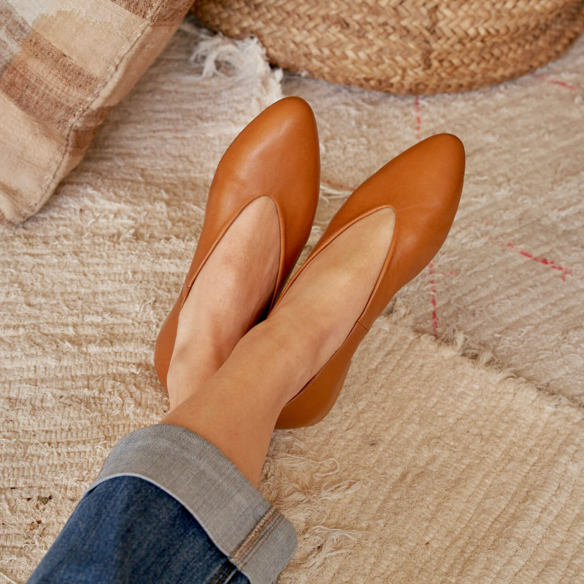 Flat ballerina in tan color, close-up view of crossed feet, resting on a rug - MONPIEL