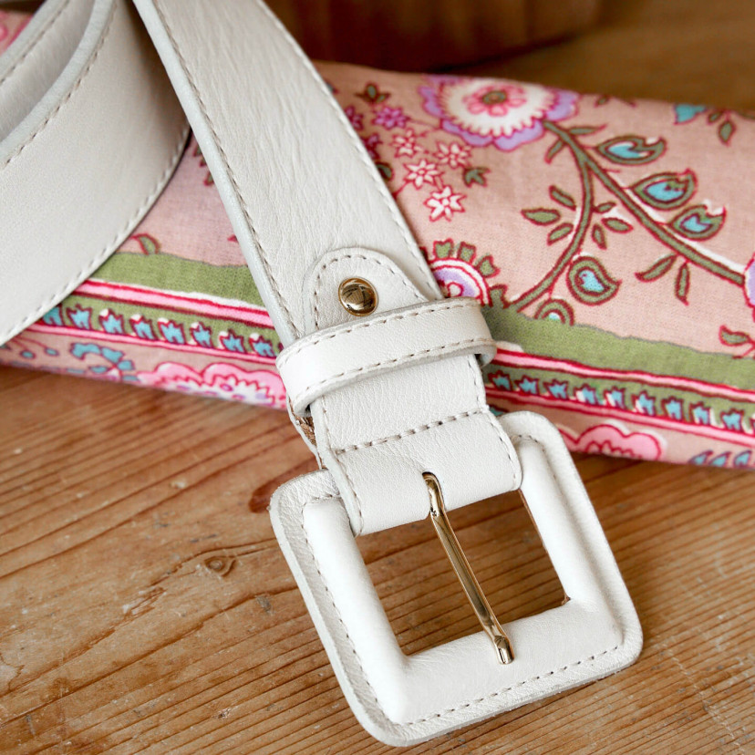 Wide women's leather belt with covered buckle in beige color, close-up of the buckle detail, resting on a wooden table - MONPIEL
