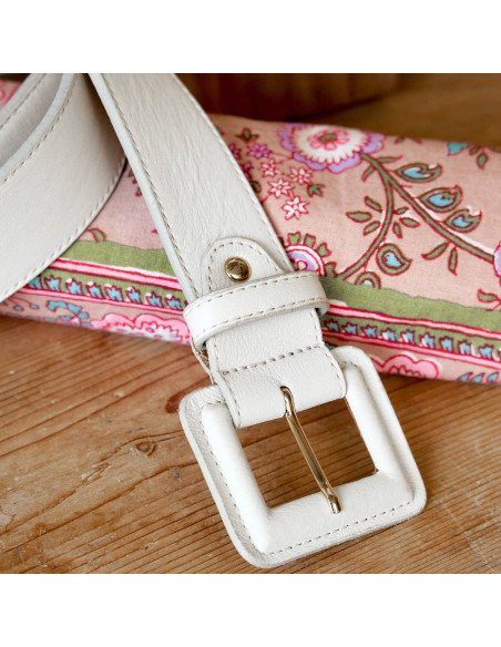 Wide leather women’s belt with covered buckle in beige, close-up of the buckle resting on a wooden table - MONPIEL Wide leather women’s belt with covered buckle in beige, close-up of the buckle resting on a wooden table - MONPIEL