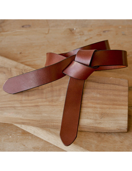 Vaquetilla leather knot belt in tan color, on a wooden table - MONPIEL Vaquetilla leather knot belt in tan color, on a wooden table - MONPIEL