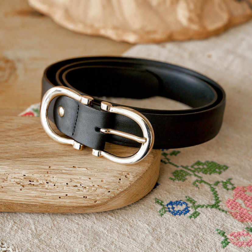 Women’s double buckle leather belt in black, coiled on a wooden board - MONPIEL