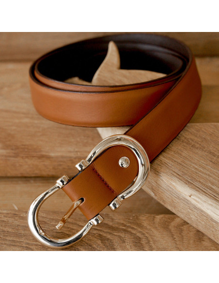 Women’s double buckle leather belt in tan, coiled and resting on a wooden board - MONPIEL Women’s double buckle leather belt in tan, coiled and resting on a wooden board - MONPIEL