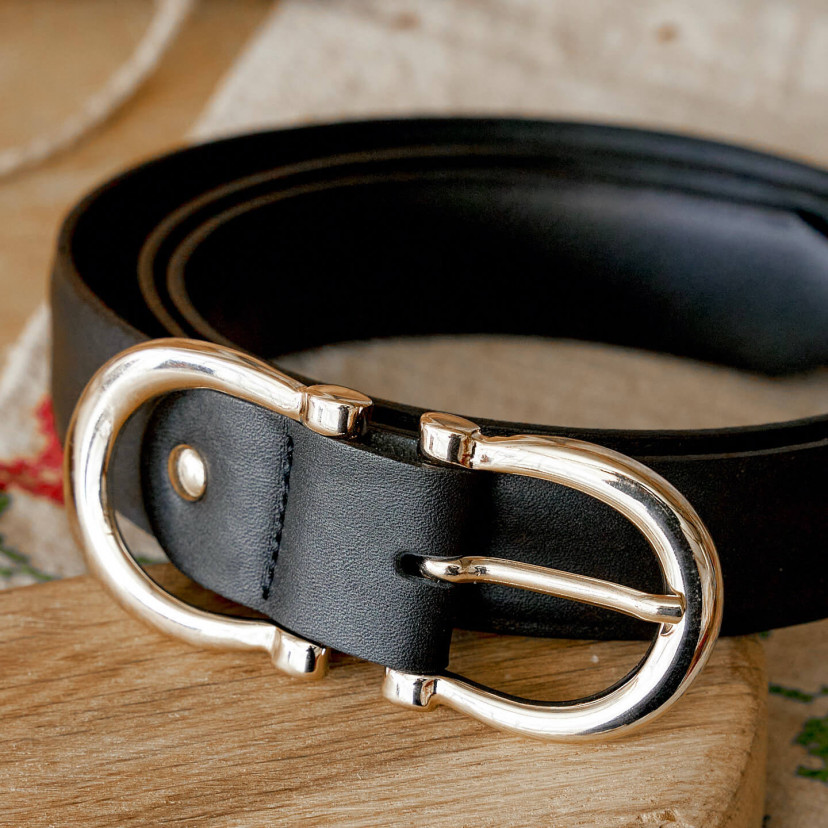 Women’s double buckle leather belt in black, coiled on a wooden board, buckle in close-up - MONPIEL