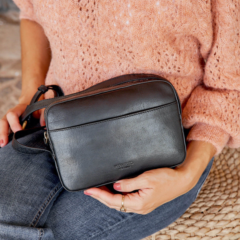 Bolsa tiracolo de couro em preto com vista frontal e segurado com a mão - MONPIEL