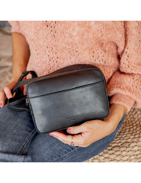 Leather crossbody bag in black, front view, held by hand - MONPIEL Leather crossbody bag in black, front view, held by hand - MONPIEL