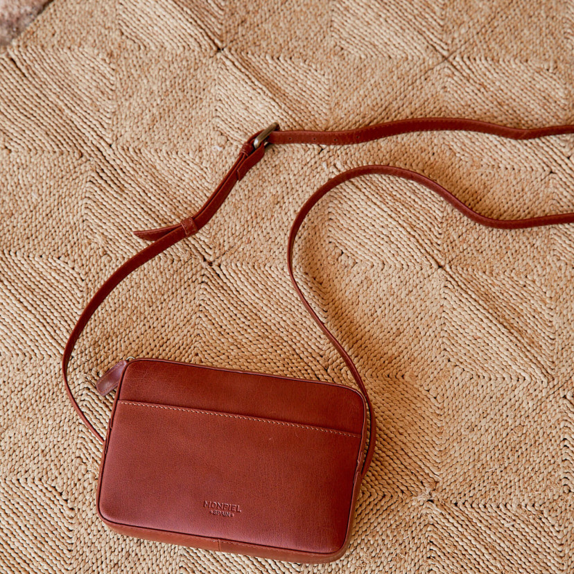 Bolsa tiracolo de couro em cor couro com vista frontal e detalhe de alça ajustável sobre tapete - MONPIEL