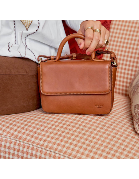 Small Armado leather purse in tan color, front view on a sofa, with short strap held - MONPIEL Small Armado leather purse in tan color, front view on a sofa, with short strap held - MONPIEL