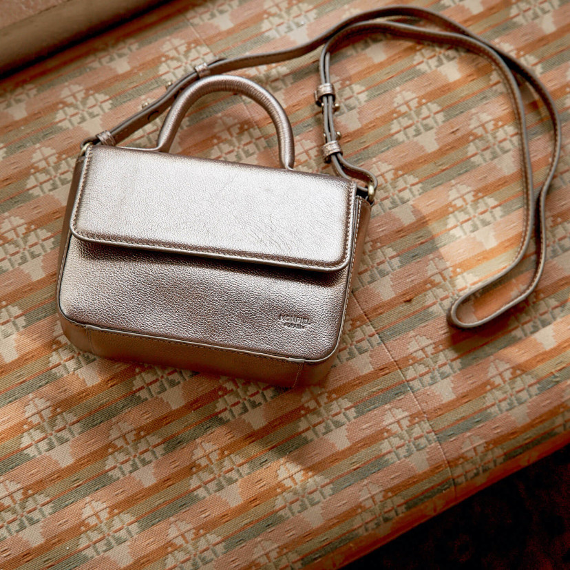 Small Armado leather bag in metallic champagne color, top and front views, resting on the sofa - MONPIEL