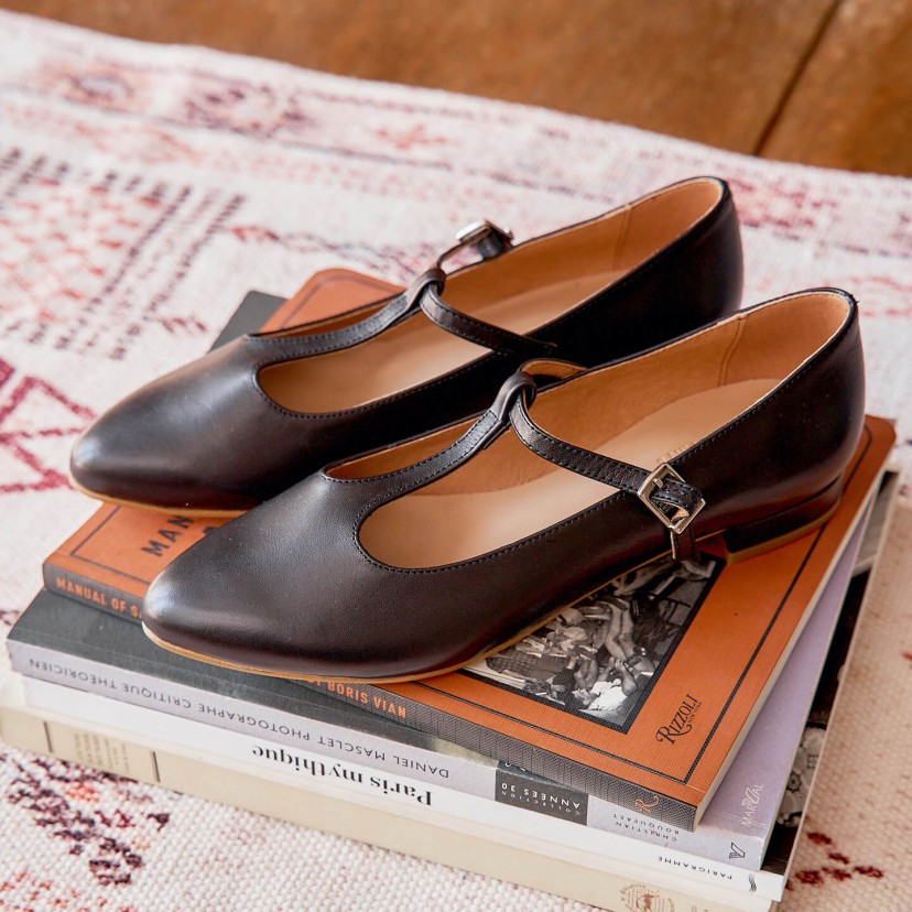 Marieta leather Mary Janes for women in black color, angled view, resting on books - MONPIEL