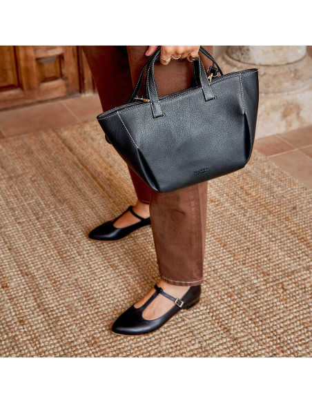 Mary Janes femininas Marieta de couro preto, plano médio com vista desfocada e bolsa preta de couro na mão - MONPIEL