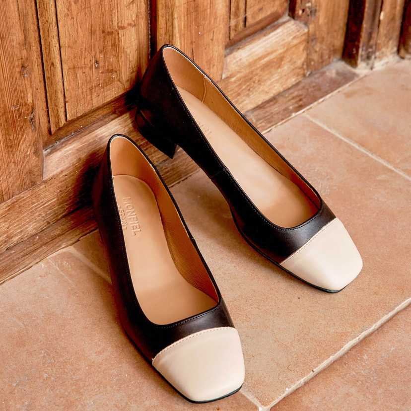 Women’s square-toe leather shoes in black with beige toe cap, resting on a wooden door - MONPIEL