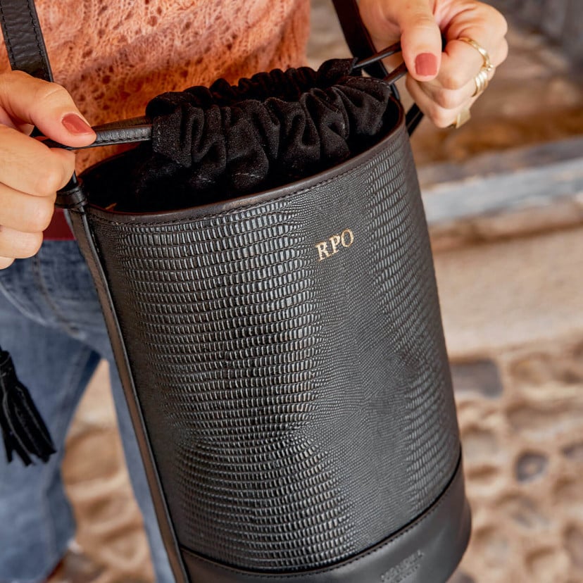 Three gold-embossed initials on a black leather bucket bag with snake-print detail, drawstring closed - MONPIEL