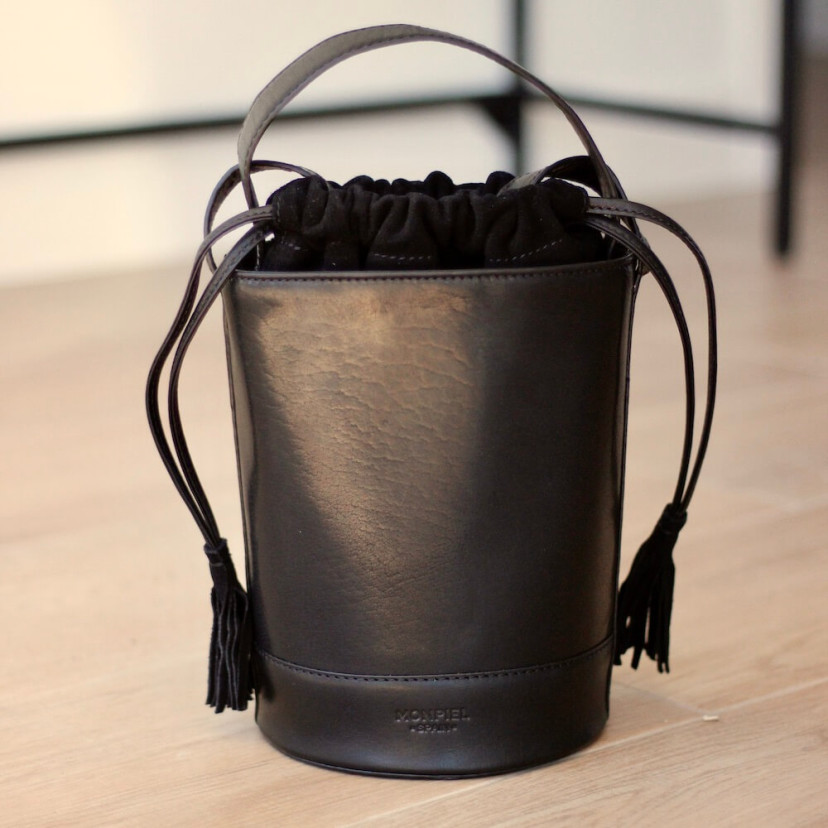 Bolsa redonda de couro pequena em preto com vista frontal apoiada no chão - MONPIEL