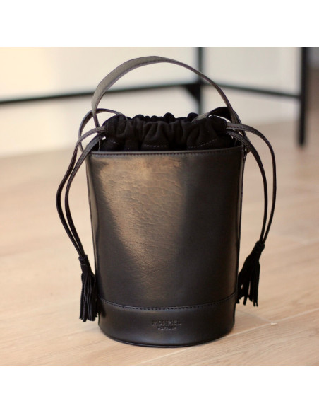 Small round leather bucket bag in black, front view, resting on the floor - MONPIEL