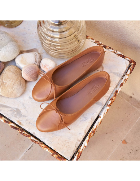 High-cut leather ballerina in tan color, top view, resting on a table next to a vase - MONPIEL High-cut leather ballerina in tan color, top view, resting on a table next to a vase - MONPIEL