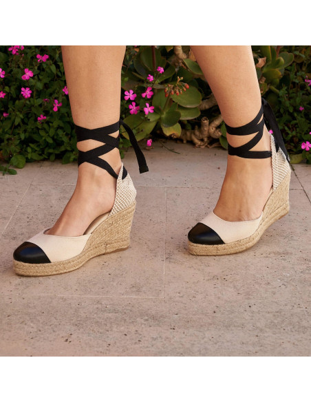 Espadrille à talon compensé en cuir noir à bout fermé, vue en perspective de pas, fond de fleurs - MONPIEL Espadrille à talon compensé en cuir noir à bout fermé, vue en perspective de pas, fond de fleurs - MONPIEL