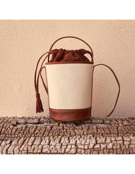 Small canvas bucket bag in tan, front view, resting on a tree trunk - MONPIEL Small canvas bucket bag in tan, front view, resting on a tree trunk - MONPIEL