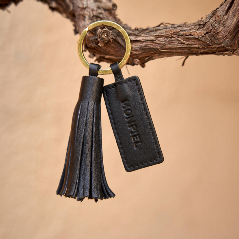Black leather tassel keychain with logo detail, hanging from a branch - MONPIEL