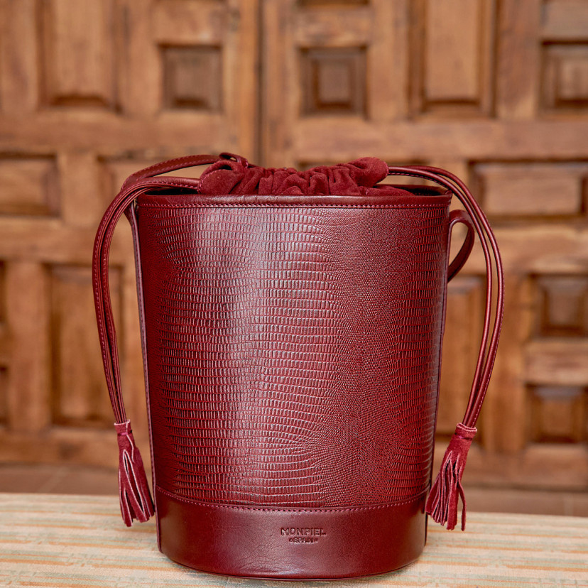 Bolsa redonda em formato de cubo de couro em estampa de cobra bordô, vista frontal na frente de uma porta de madeira - MONPIEL