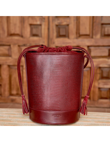 Bolso redondo en forma de cubo de piel en color serpiente burdeos con vista frontal delante de puerta de madera - MONPIEL