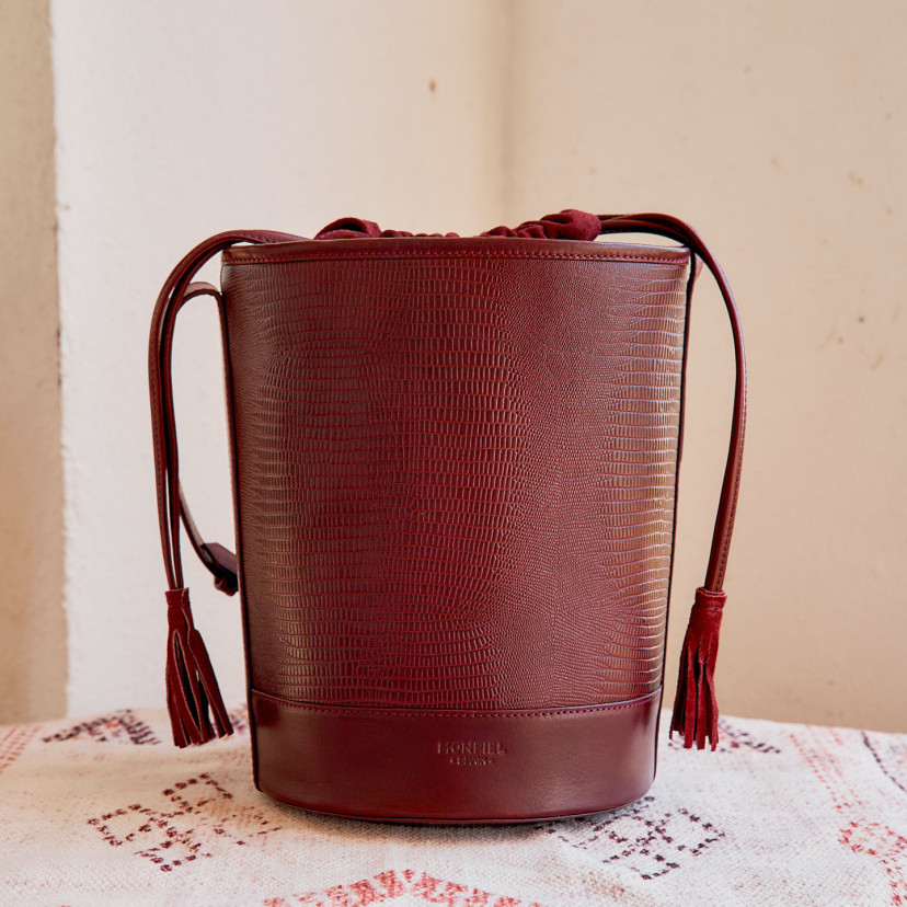 Bolsa redonda em formato de cubo de couro em estampa de cobra bordô, vista frontal sobre um tapete - MONPIEL
