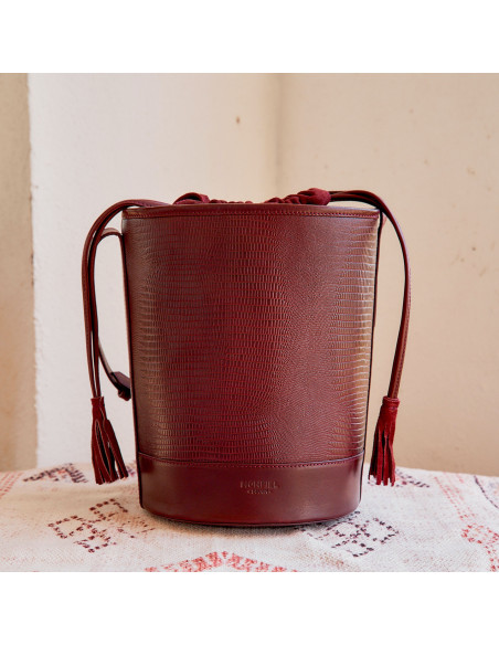 Round leather cube-shaped bag in burgundy snake print, front view on a rug - MONPIEL