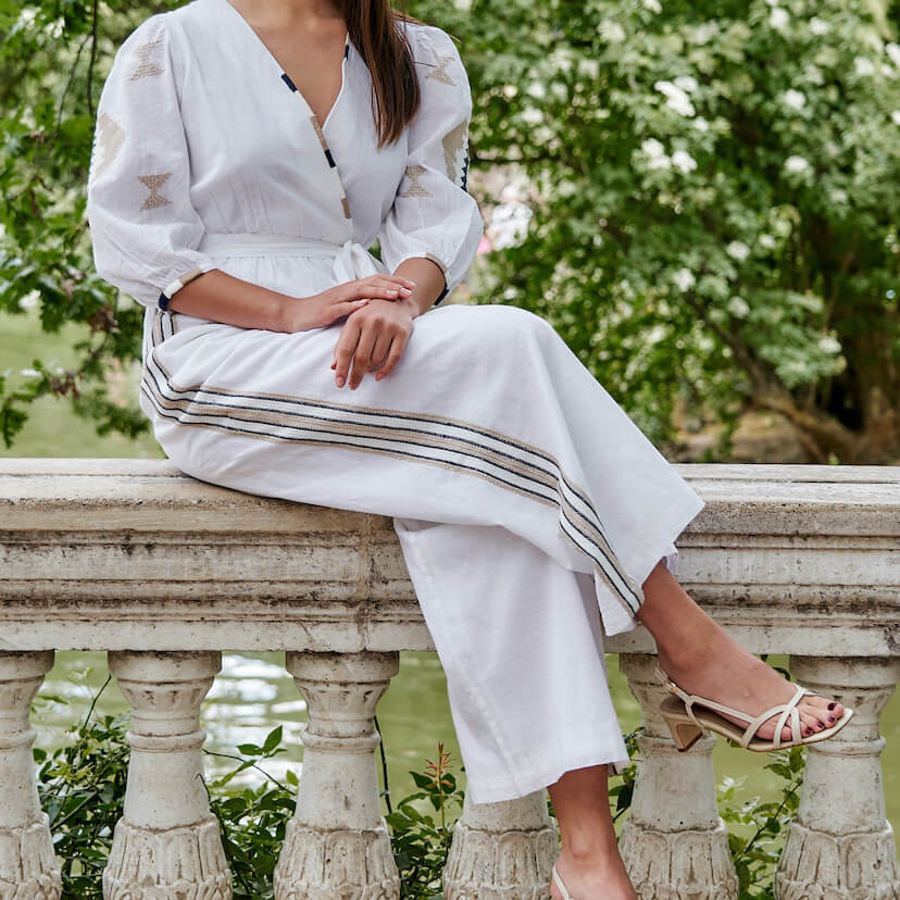 Hand-embroidered white ethnic jumpsuit, legs crossed, seated on a wall - MONPIEL