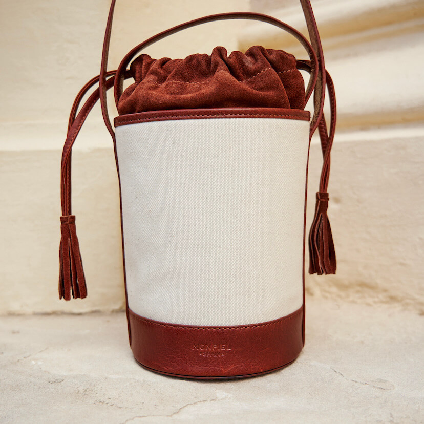 Bolsa cubo pequena de canvas em tom couro com vista frontal apoiada em um muro - MONPIEL