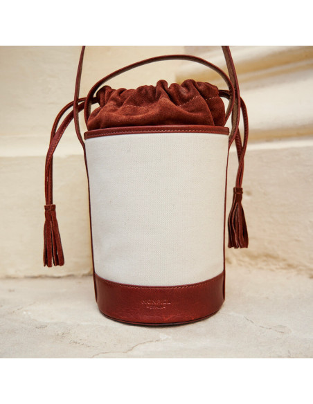 Small canvas bucket bag in tan, front view, resting on a wall - MONPIEL Small canvas bucket bag in tan, front view, resting on a wall - MONPIEL