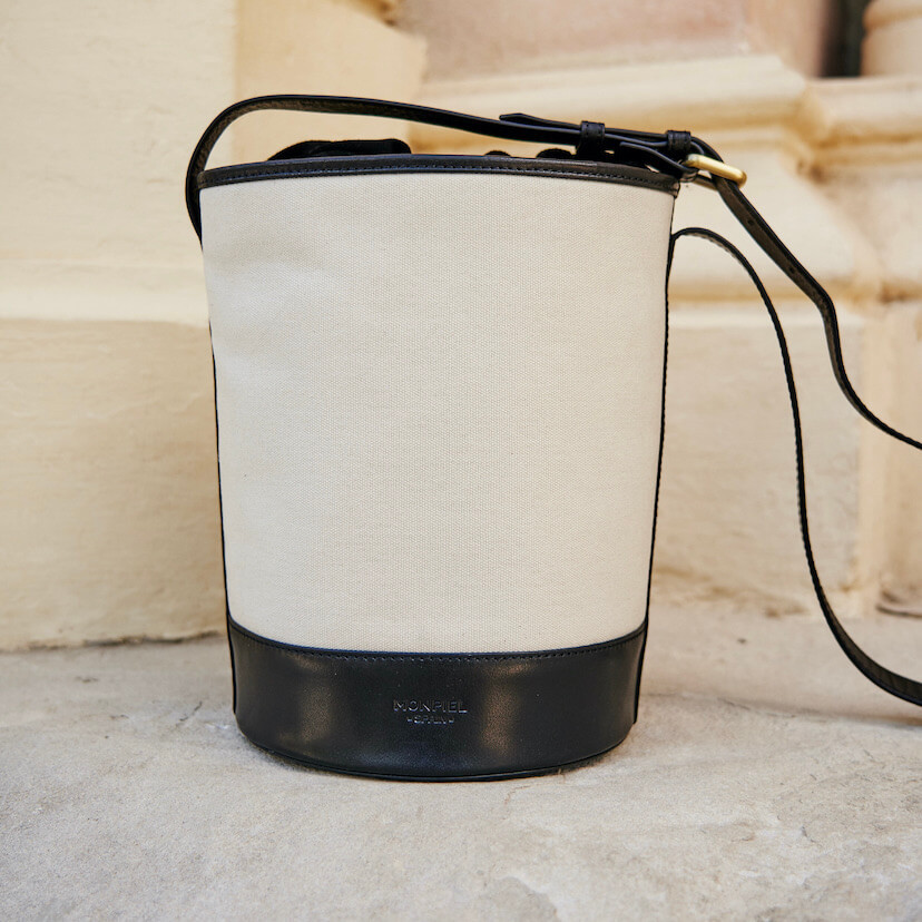 Bolsa cubo de canvas e couro preto com vista frontal apoiada em um muro - MONPIEL