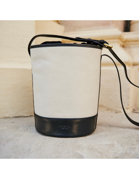 Canvas leather bucket bag in black color, front view, resting on a wall - MONPIEL Canvas leather bucket bag in black color, front view, resting on a wall - MONPIEL