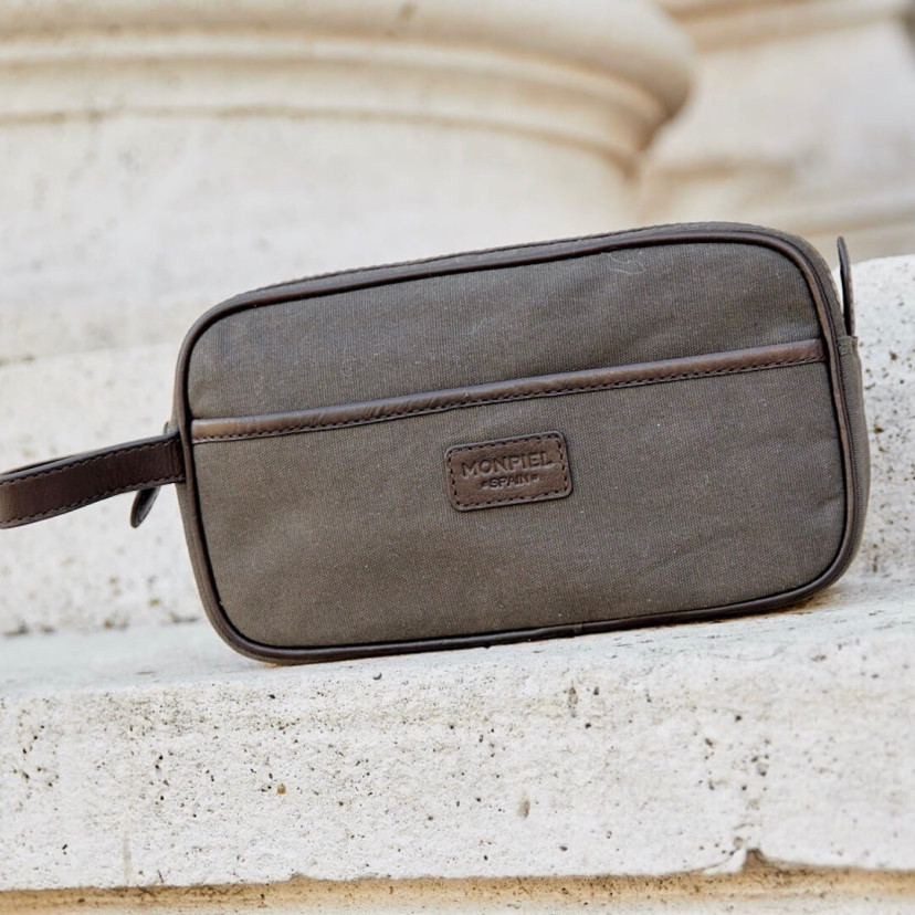 Necessaire masculino de canvas e couro em verde, com vista frontal apoiado em um muro - MONPIEL