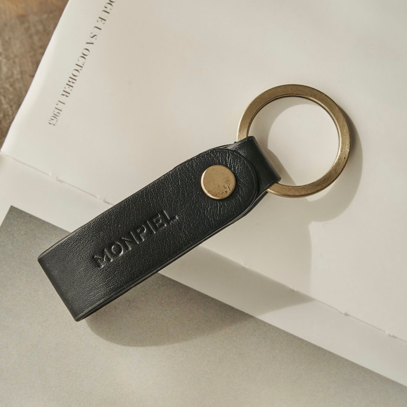 Unisex leather keychain in black color, slightly tilted, resting on a magazine - MONPIEL